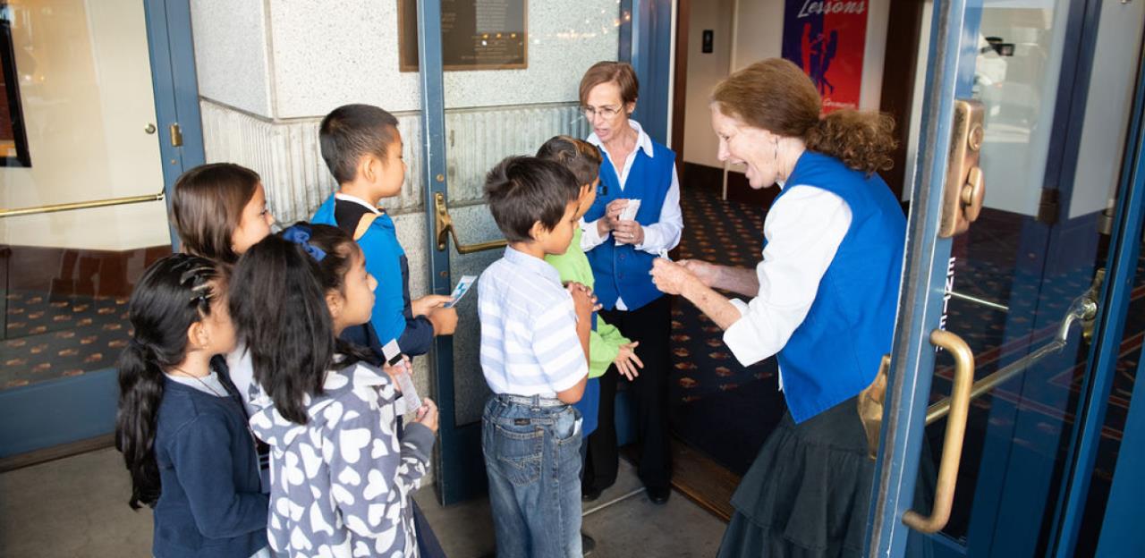 Two ushers welcoming a group of young students into the Center